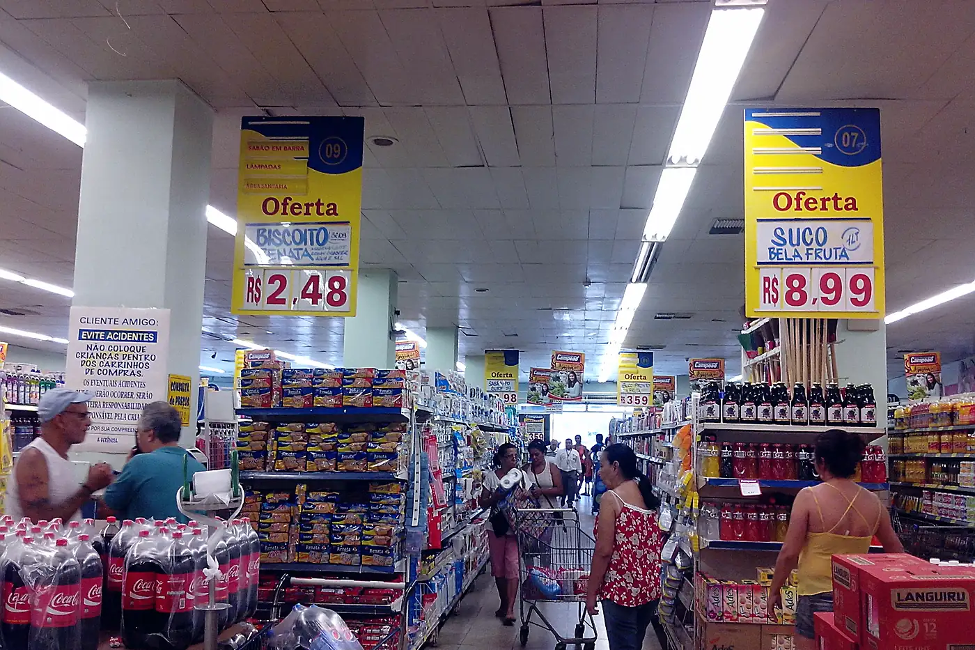 Corredor de supermercado popular com clientes e placas de oferta em reais